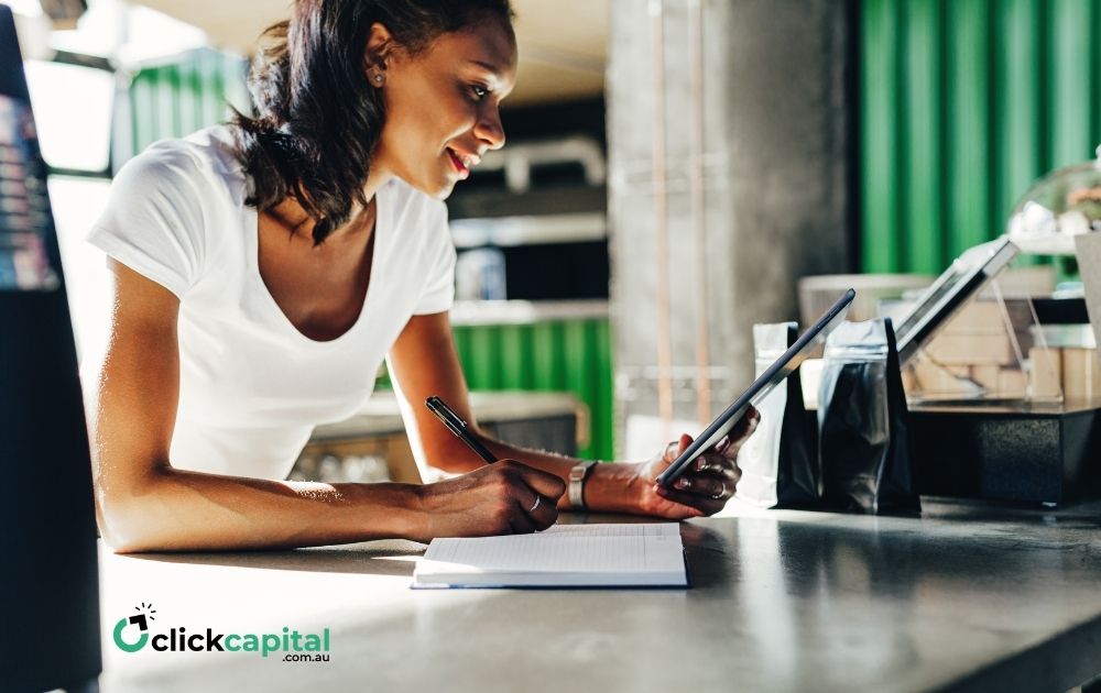 young business owner reviewing her competitors on a tablet while taking down notes