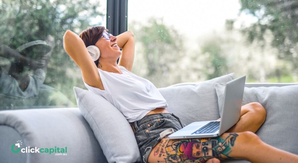 woman relaxing on couch while on headphones and laptop