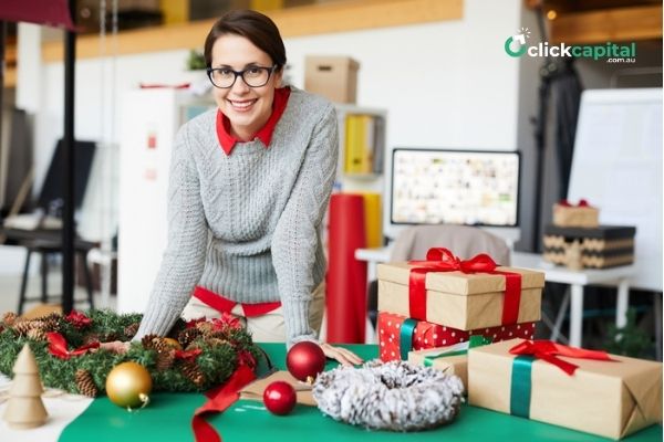 Happy business woman in grey knitted sweater leaning over table with Christmas decorations in her shop